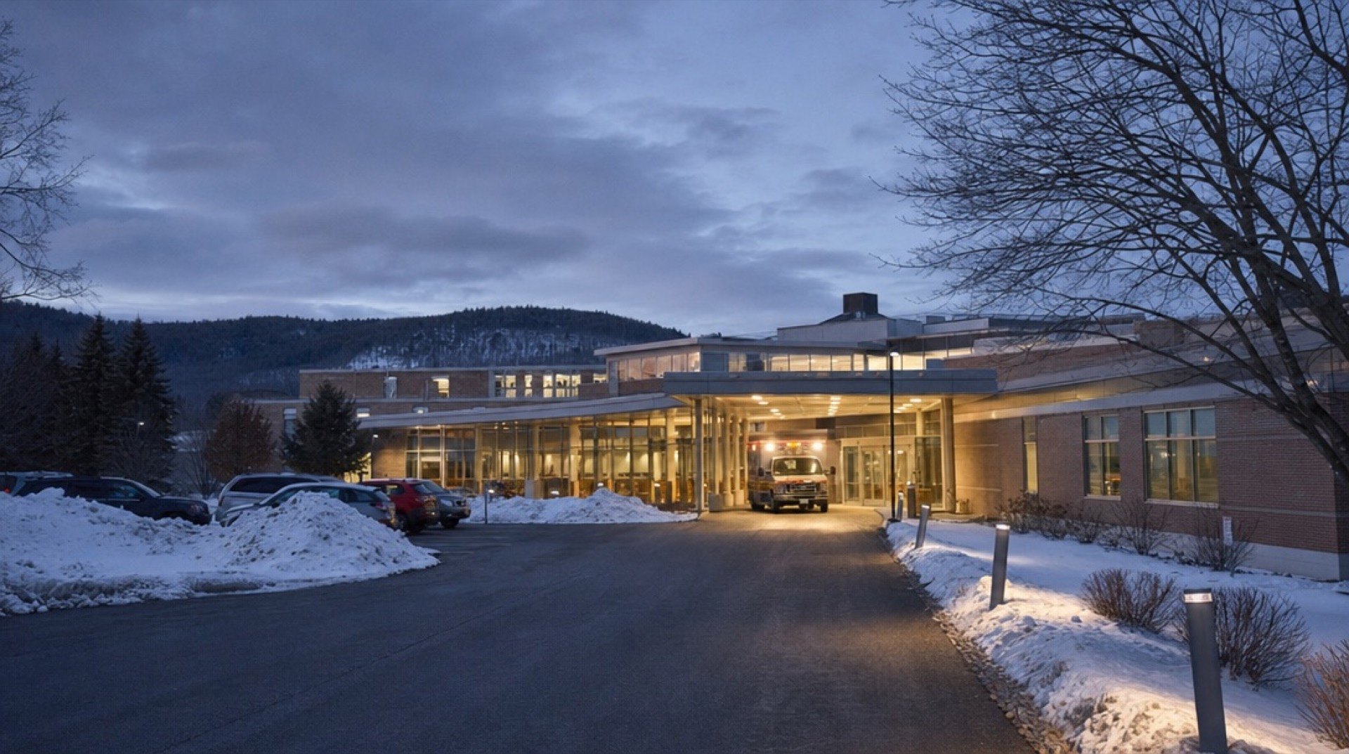 A small rural hospital at dusk in early winter, with an ambulance at the emergency entrance