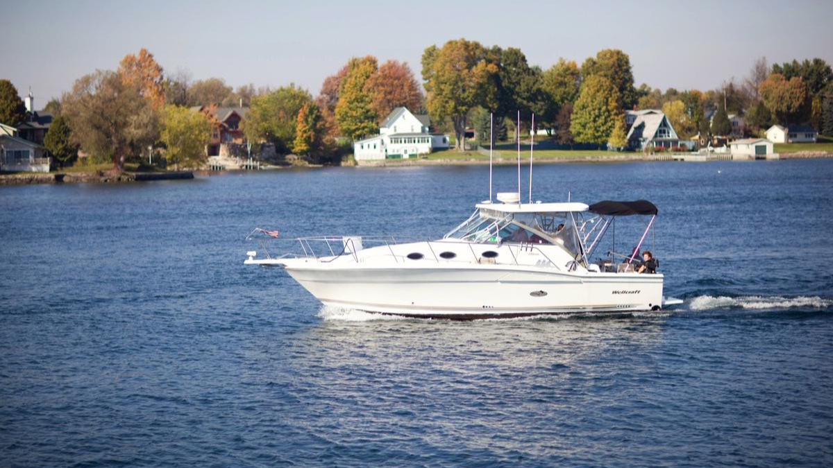 A white charter boat cruising past fall-colored trees and cottages on the river