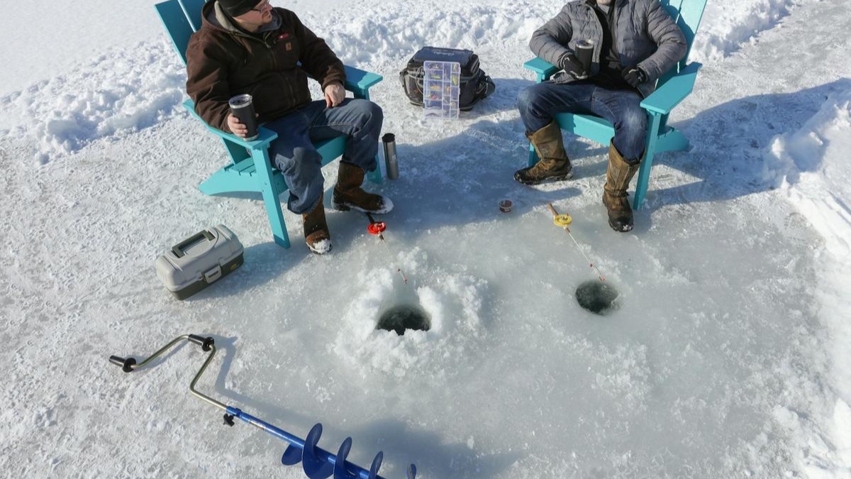 Two anglers in chairs beside drilled holes in the ice, with a hand auger in the foreground